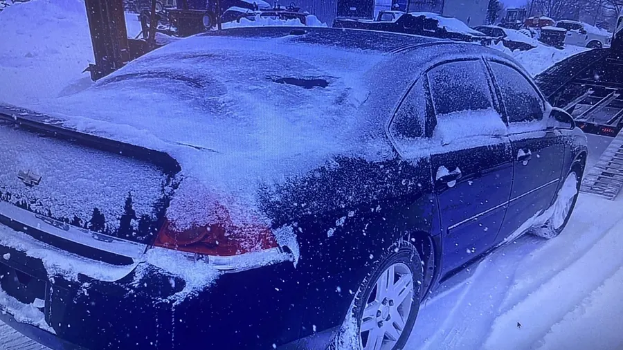 Snow-covered sedan picked up for transport in winter weather
