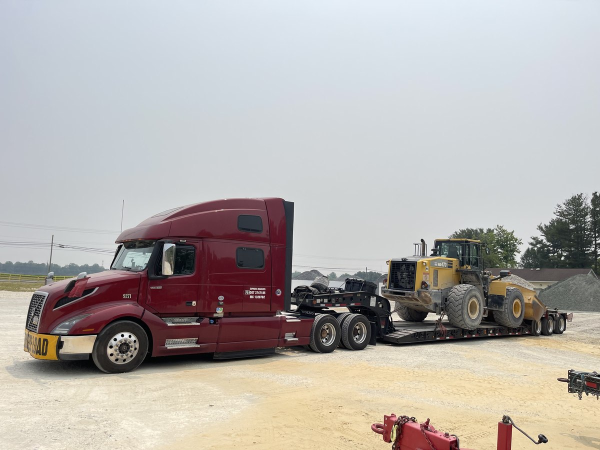 Red Volvo tractor with a wheel loader on a lowboy trailer