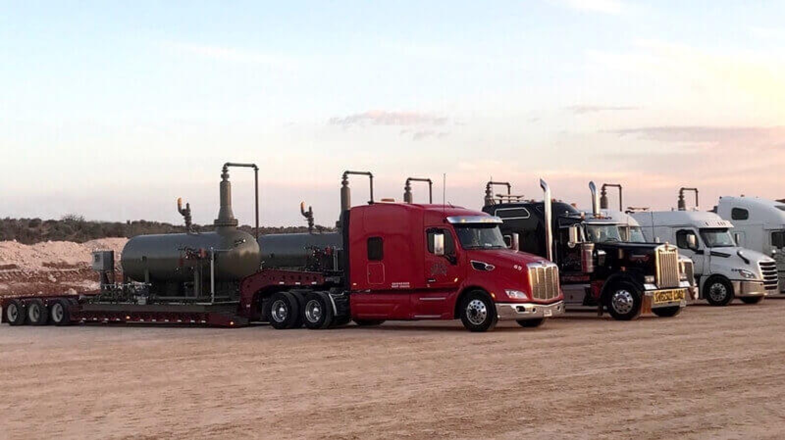 ETG lowboy rigs hauling tank equipment at sunset