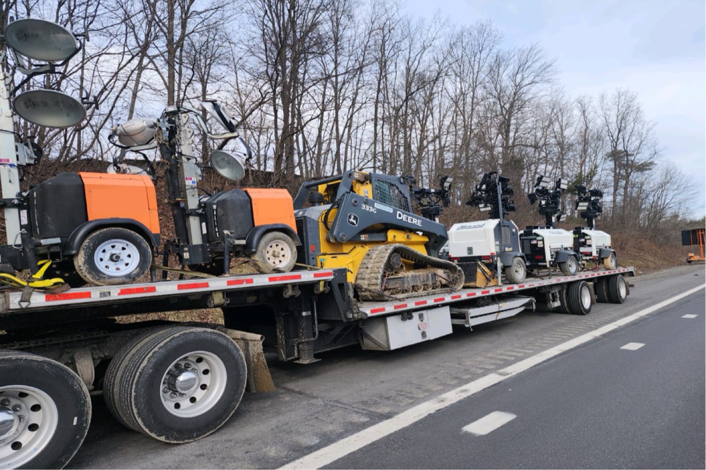Skid steer and light towers secured on a stepdeck trailer